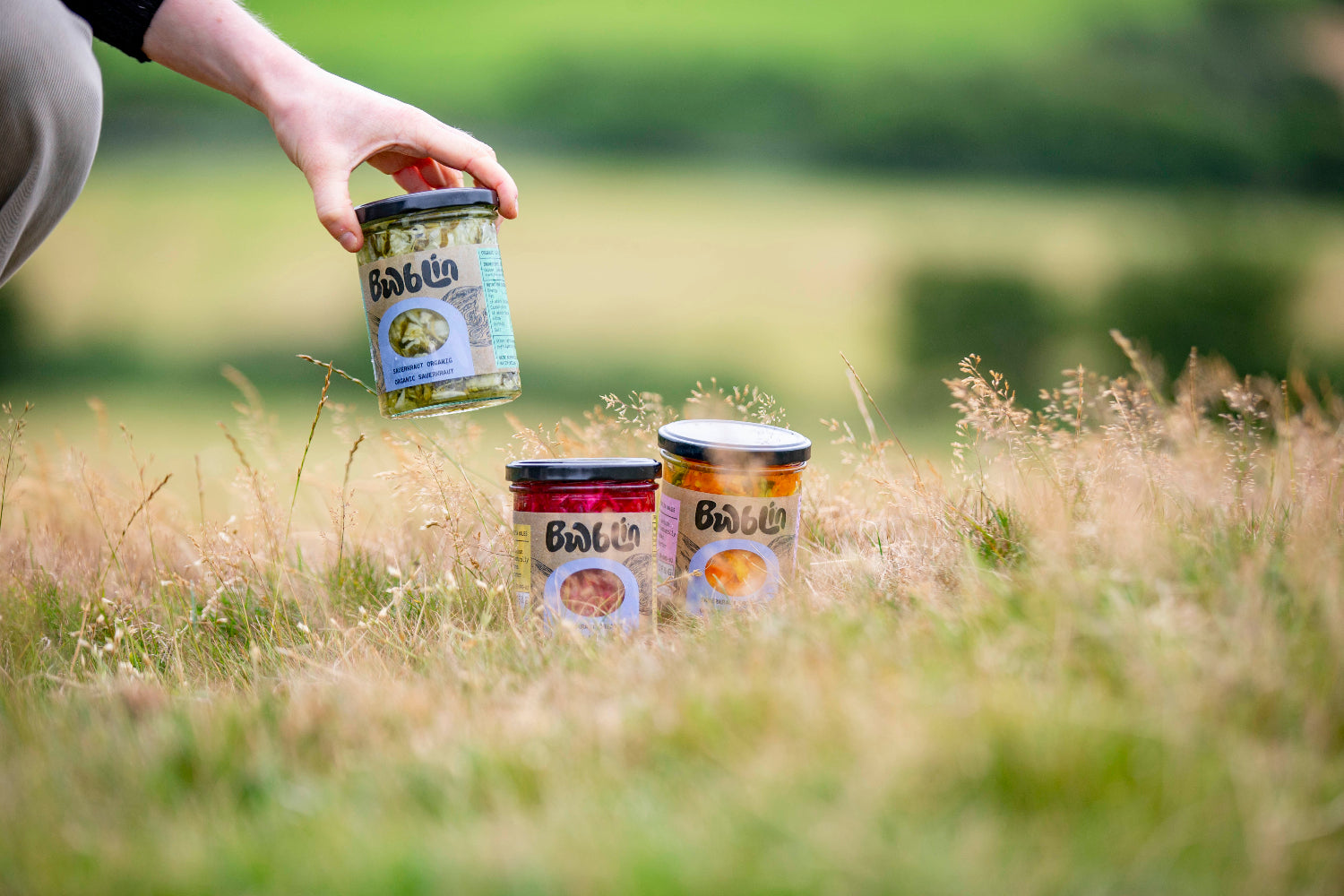 Person holding a jar of food in a grassy outdoor setting