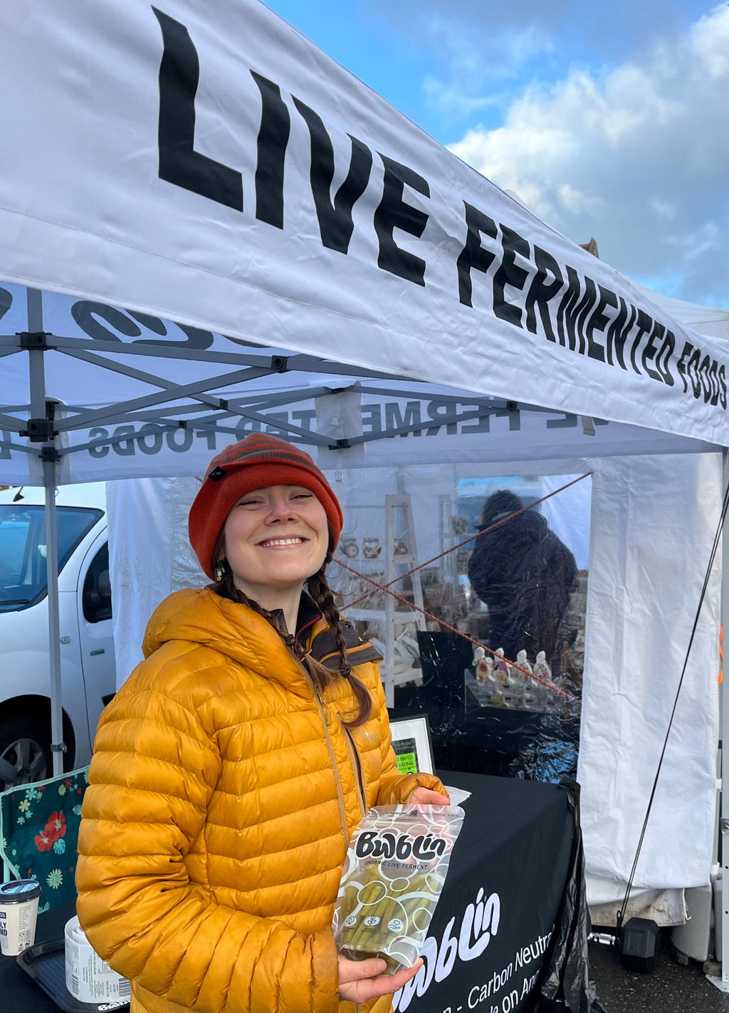Person holding a product under a 'Live Fermented Dilly beans' tent