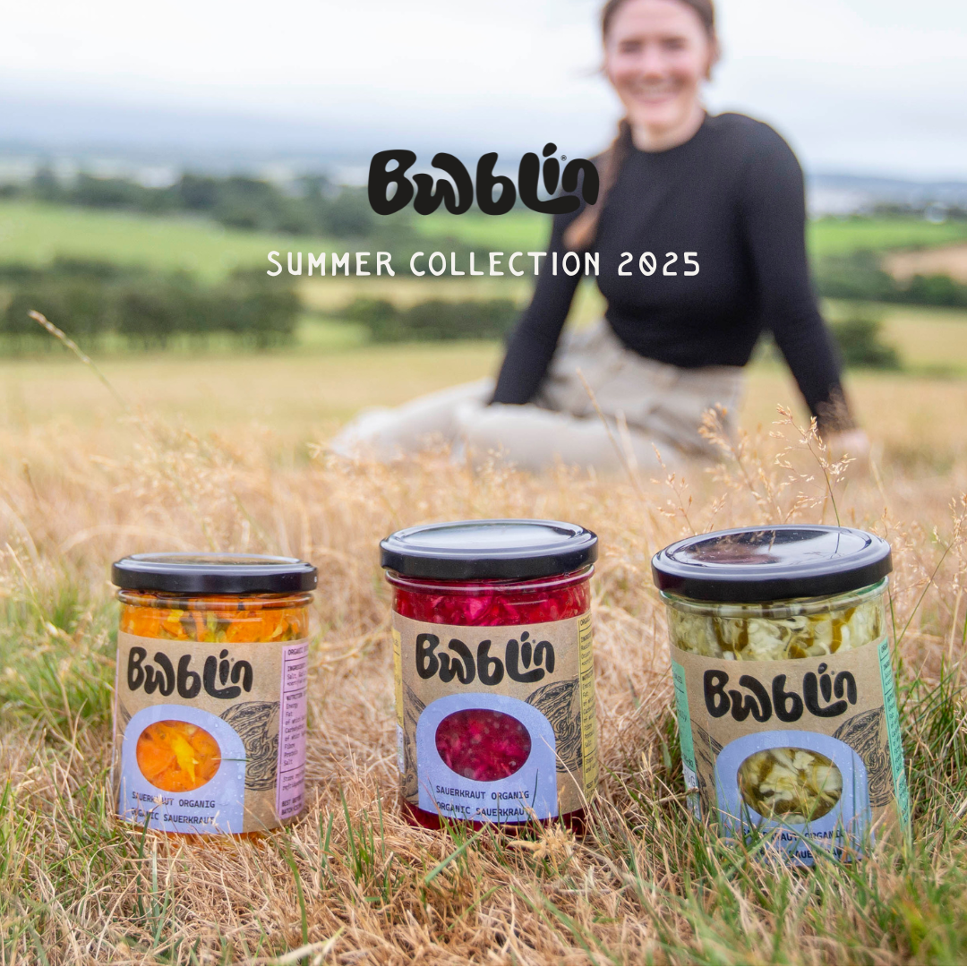 Three jars with labels on grass, with a person sitting in the background and 'Bwblin' branding.