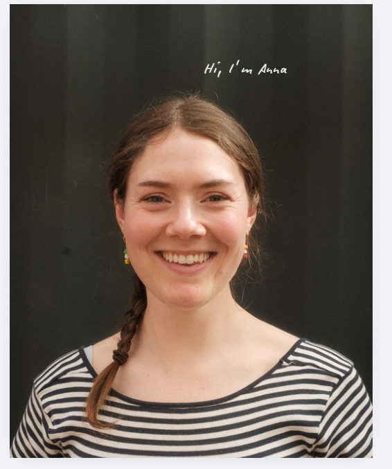 A smiling woman with brown hair in a side braid, wearing a black and white horizontally striped top, photographed against a dark background with the text 'Hi! I'm Anna' at the top.
