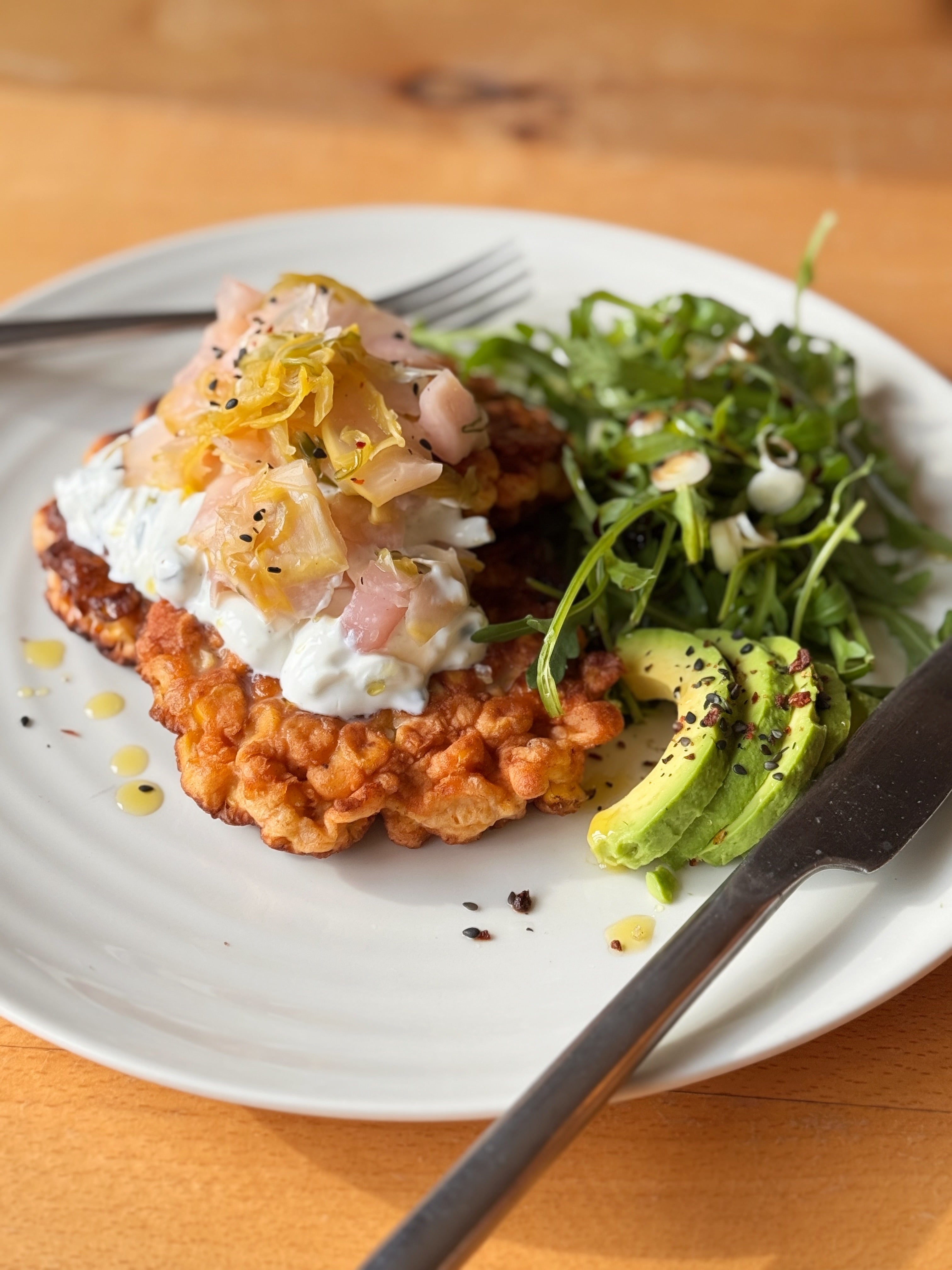 Plate of food with a fried dish, salad, and avocado on a wooden table.