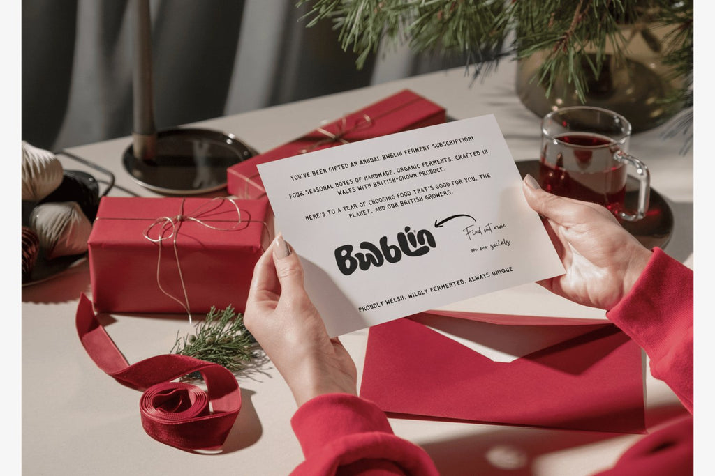 Person holding a card with 'Babblin' on it at a festive table with red gift boxes and a cup of tea.