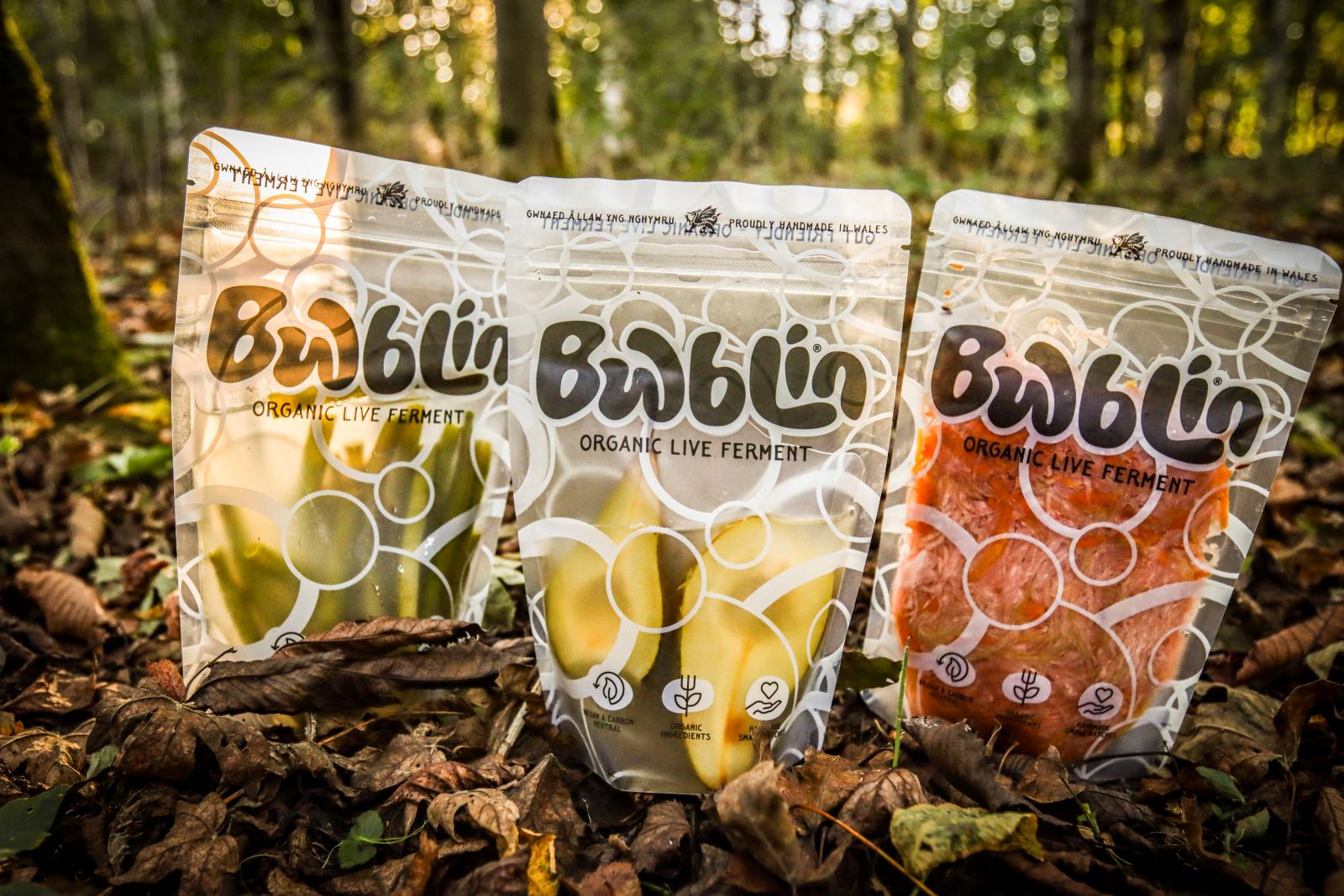 Three packages of Bwblin organic live ferments on a leafy ground with a forest background.