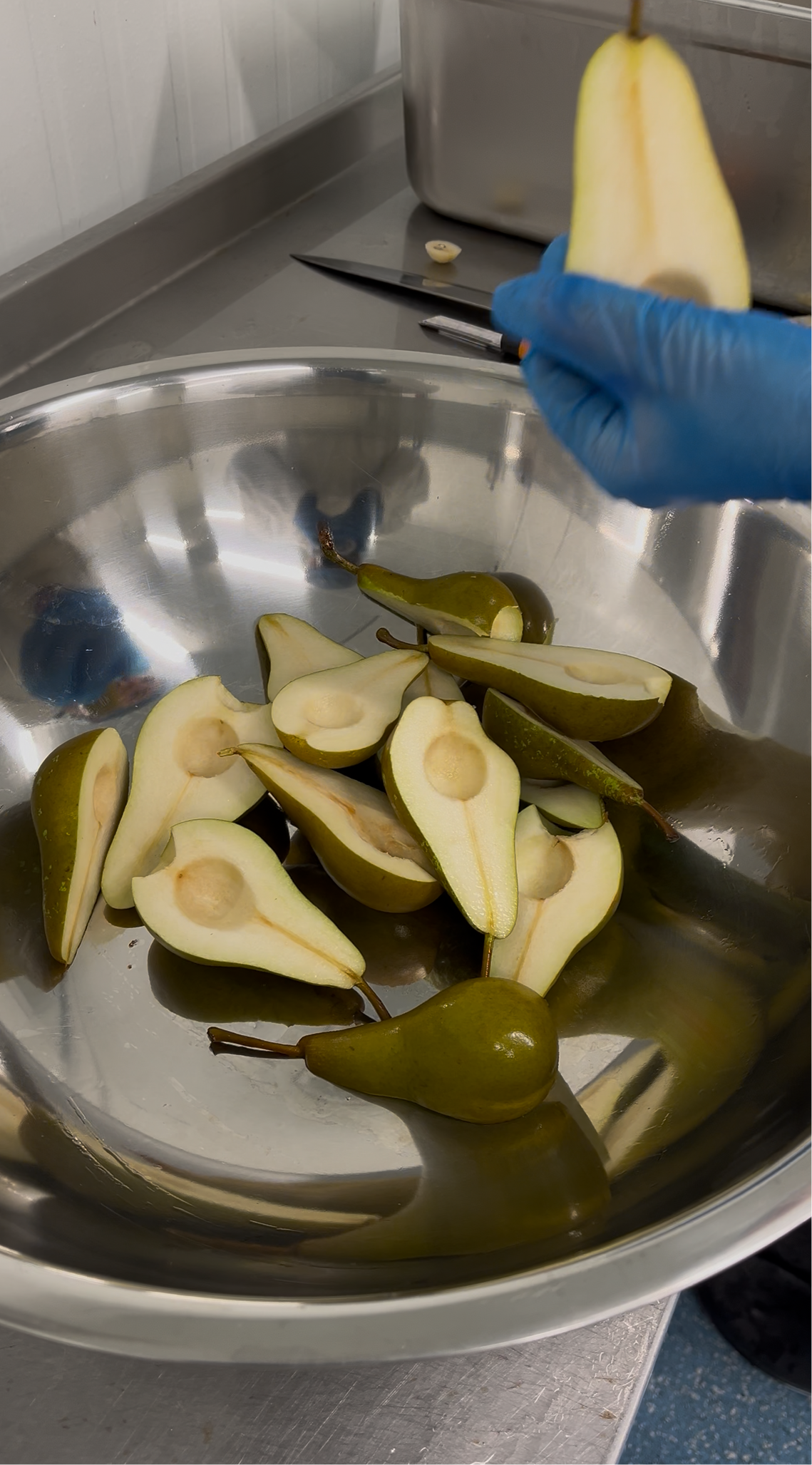 Pears being cut on a metal surface with a hand wearing a blue glove.
