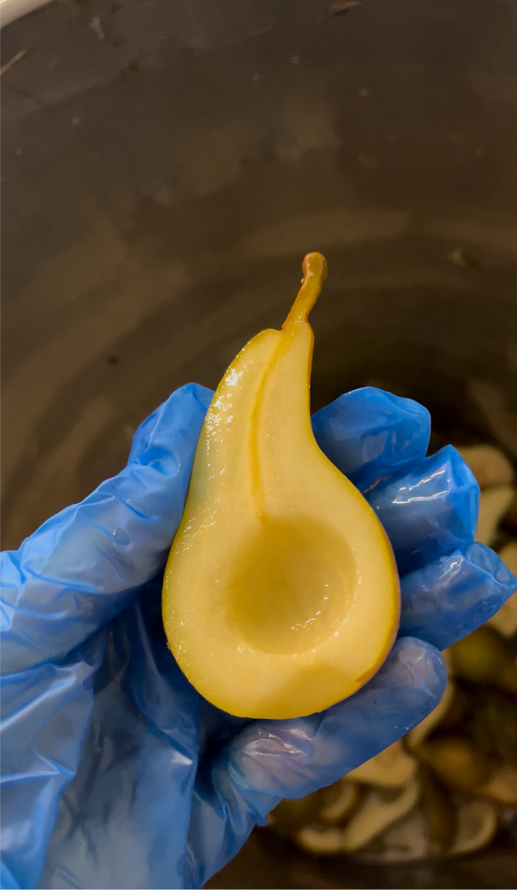 Yellow candle shaped like a pear held by a gloved hand against a dark background