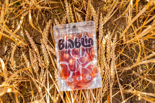 A clear stand-up pouch of red radishes a white and black 'Bwblin' logo, placed on a background of dry golden wheat stalks.